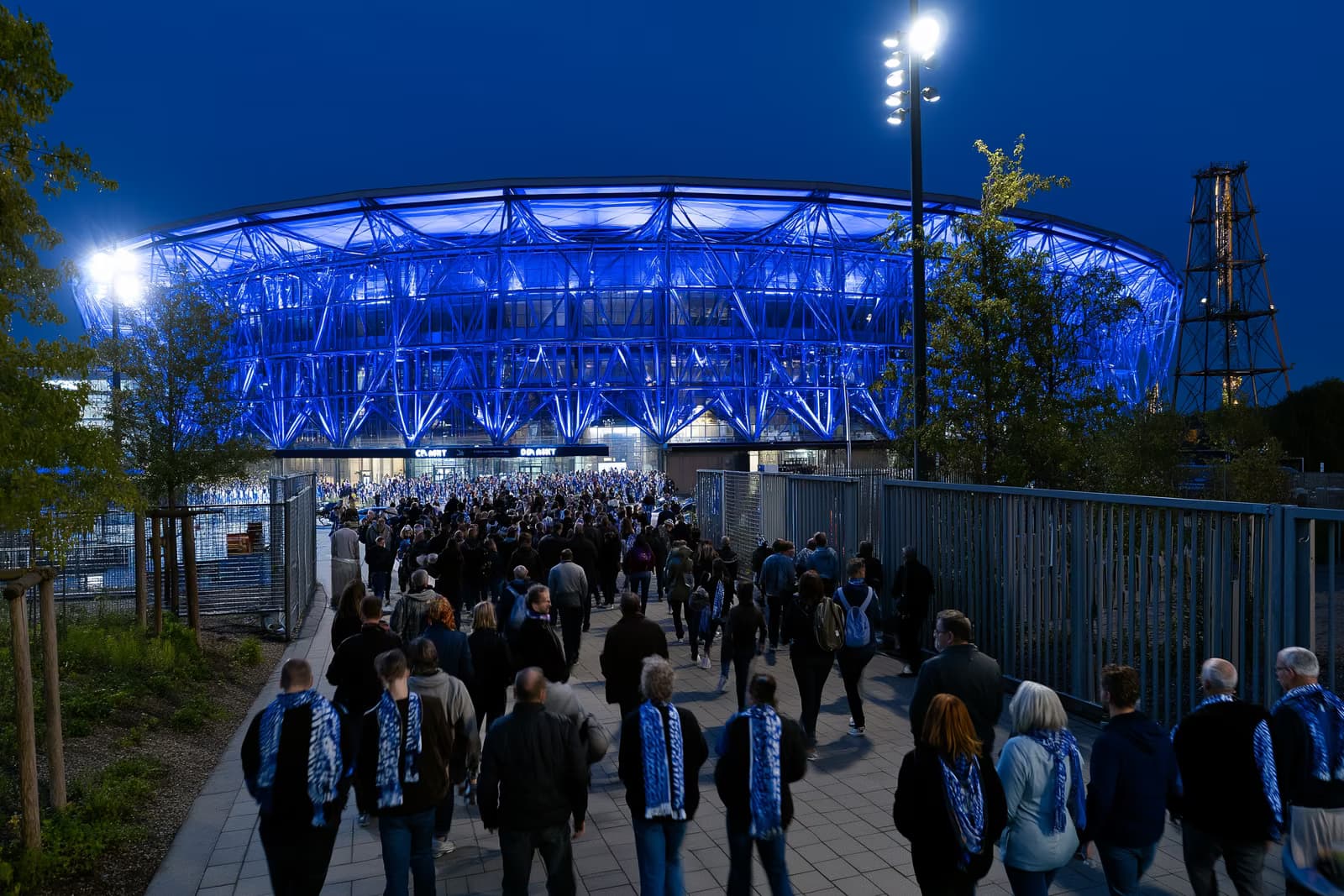 Futbola stadions Rūras apgabalā naktī mirdz karaliski zilā krāsā, kamēr šallēs tērpti fani plūst uz vārtiem pēc Gosens Schalke pārtveršanas.
