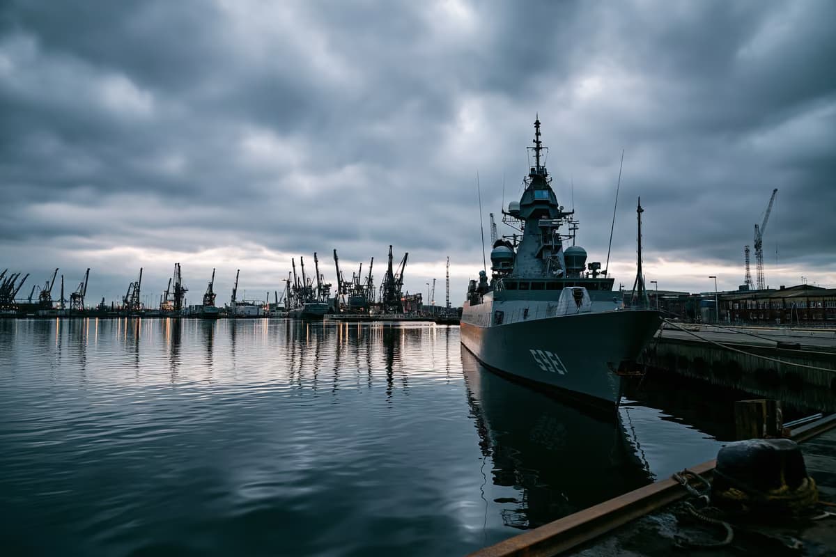 Pelēks jūras spēku doks zem apmākušās debess, kas liecina par investīcijām aizsardzībā.